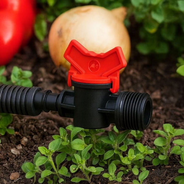 Kunststoff-Absperrventil für die Gartenbewässerung mit rotem Drehgriff in einem Gemüsebeet.