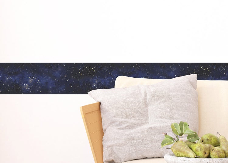 Tapetenbordüre mit Sternenhimmel-Motiv auf einer hellen Wand in einem modern eingerichteten Zimmer mit Sessel und Tischchen.