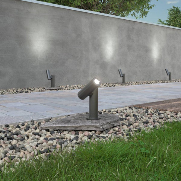 Moderne Garten-Spotlights zur Akzentbeleuchtung an einem gepflasterten Weg mit Kiesrand und Betonmauer.