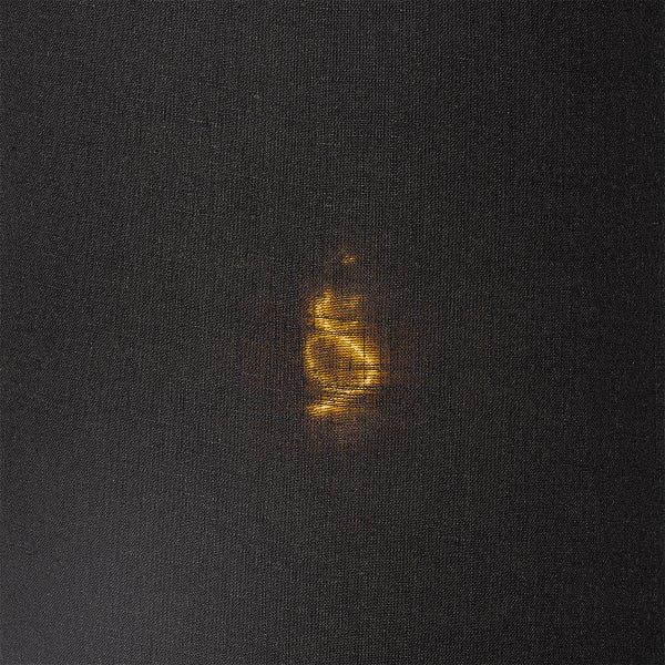 Nahaufnahme eines Lampenschirms aus dunklem Stoff mit durchscheinendem warmem Licht, das die feine Gewebestruktur betont.