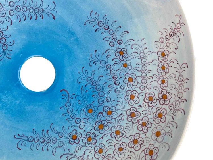 Detailansicht eines runden, hellblauen Aufsatzwaschbeckens mit floralem Muster und Abflussloch.