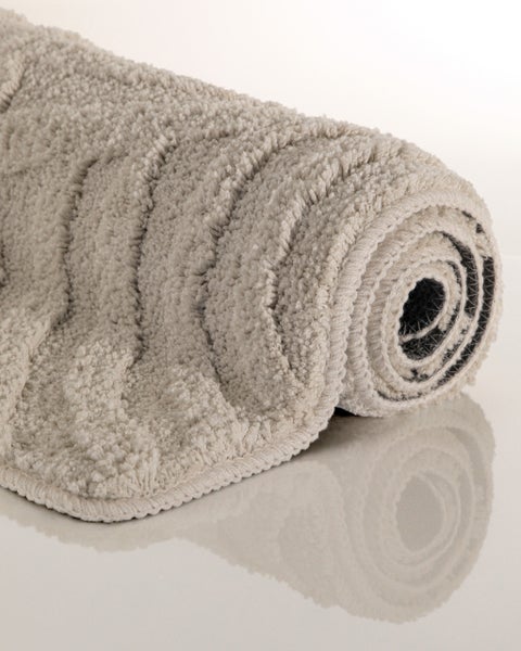 Beige zusammengerollte Badematte mit Wellenstruktur und flauschiger Oberfläche.
