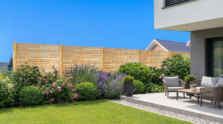 Gartenszene mit Holzzaun, Blumen und Sitzgruppe auf einer Terrasse