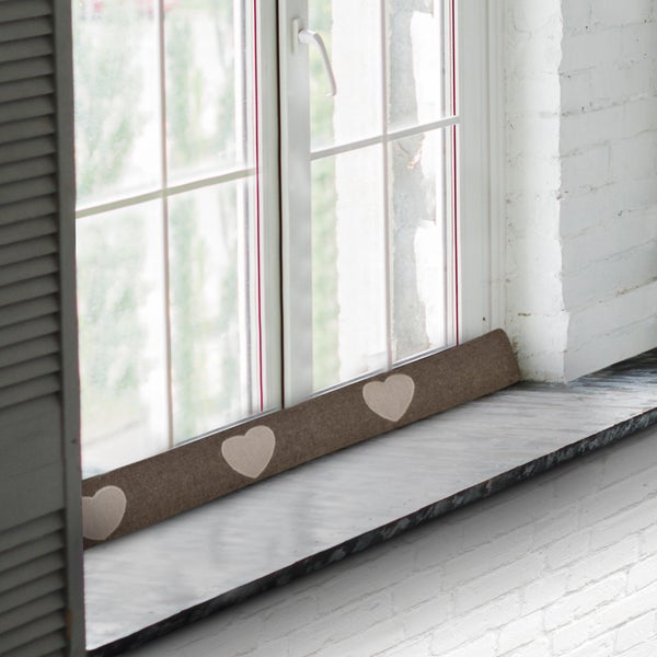 Zugluftstopper mit Herzmuster vor einem Fenster