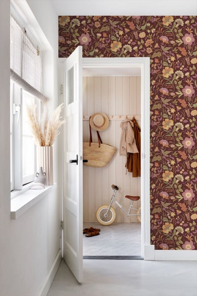 Hell gestalteter Raum mit floral gemusterter Tapete, weißer Tür und einem Blick in einen Flur mit Holzpaneelen und Garderobe.