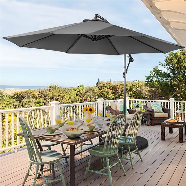 Szene mit einem Gartentisch und Stühlen unter einem grauen Sonnenschirm auf einer Terrasse mit Meerblick.