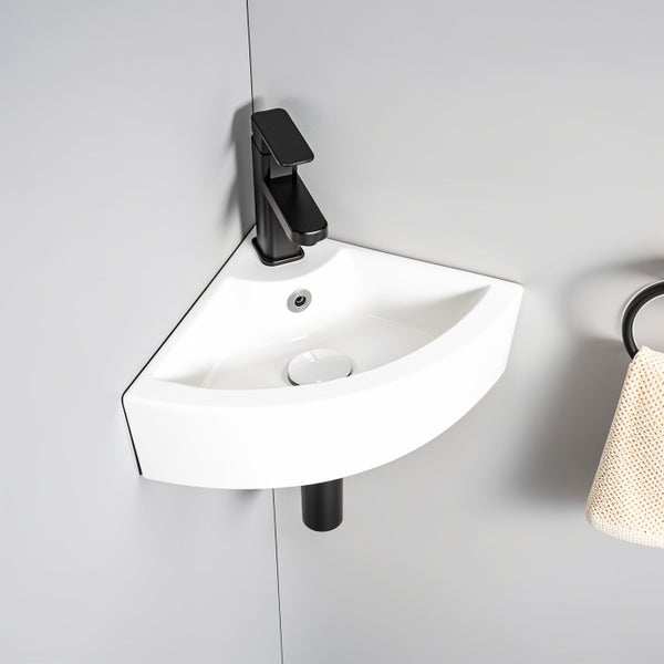 Weißes Eckwaschbecken aus Keramik mit schwarzer Einhebelarmatur und Ablaufventil, montiert an einer Badezimmerwand.