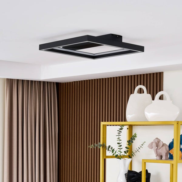 Schwarze quadratische Deckenleuchte in einem hellen Zimmer mit brauner Lamellenwand, beigen Vorhängen und einem goldenen Regal.