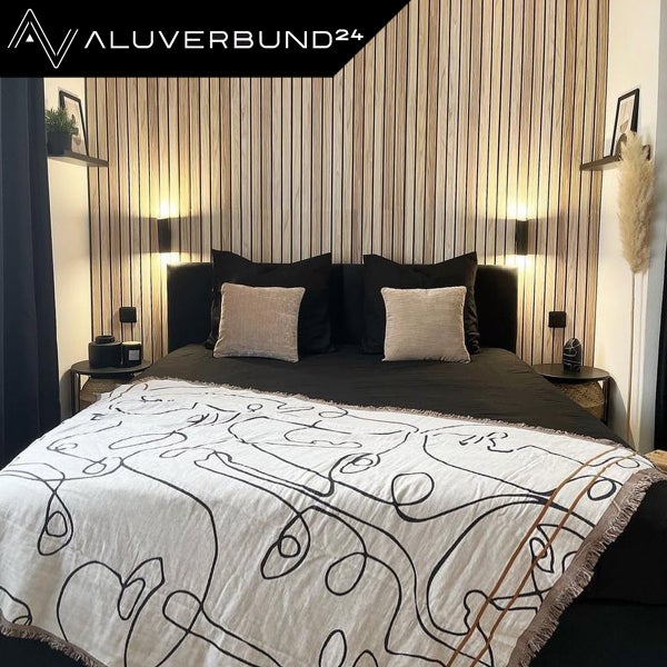 Schlafzimmer mit Bett vor einer Holzwand und Aluverbund24 Logo