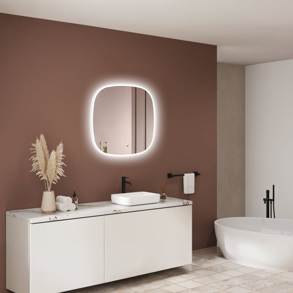 Modernes Badezimmer mit einem beleuchteten, abgerundeten Wandspiegel, einem Waschbecken auf einem Waschtisch und einer freistehenden Badewanne.
