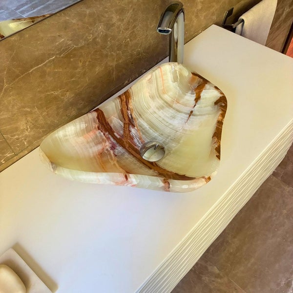 Asymmetrisches Aufsatzwaschbecken aus Naturstein mit organischer Musterung auf einem Waschtisch mit verchromter Armatur.