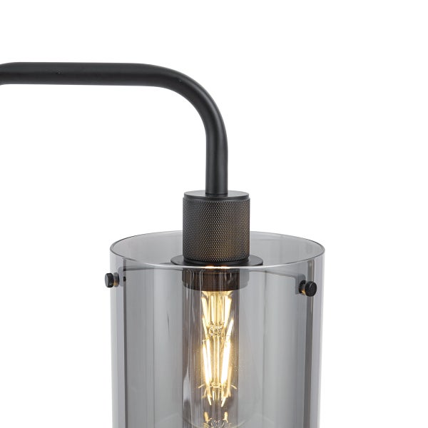 Wandleuchte mit schwarzem Metallarm, gerändelter Fassung und zylindrischem Rauchglasschirm mit Filament-Leuchtmittel.