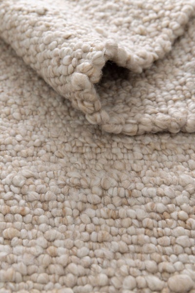Wollteppich mit grober Schlingenstruktur in Beige, Nahaufnahme mit umgeschlagener Ecke.