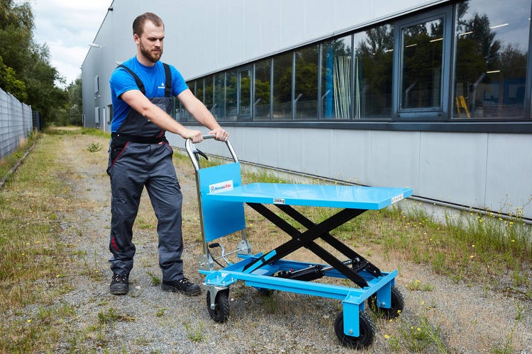 Mann schiebt einen blauen Scherenhubwagen im Aussenbereich