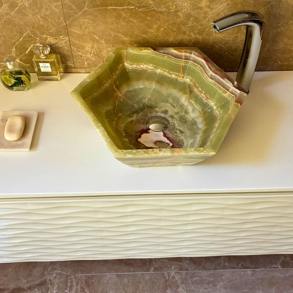 Sechseckiges Waschbecken aus Onyx mit verchromter Armatur auf einem weißen Unterschrank mit Wellenstruktur.