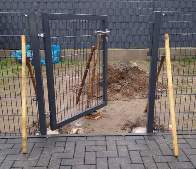 Geöffnetes Gartentor aus Metall mit Maschendrahtfüllung in einem Garten
