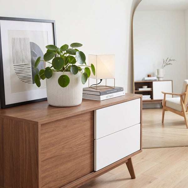 Moderne Kommode mit Holzoptik und weißen Schubladen in einem hellen, skandinavisch eingerichteten Wohnzimmer mit Pflanze, Lampe und Spiegel.