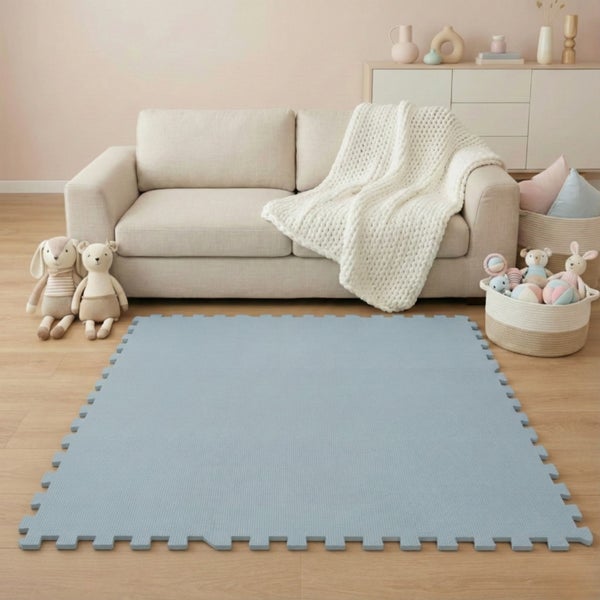 Blaue Puzzlematte aus Schaumstoff vor einem hellen Sofa im Wohnzimmer, dekoriert mit Kuscheltieren und einer weißen Strickdecke.