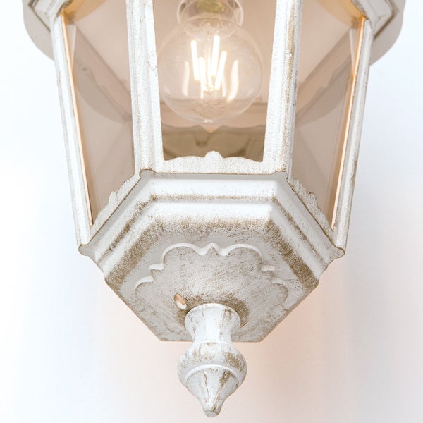 Außenwandleuchte in Laternenform aus weiß-goldfarbenem Metall mit Glaseinsätzen und eingeschaltetem Leuchtmittel.