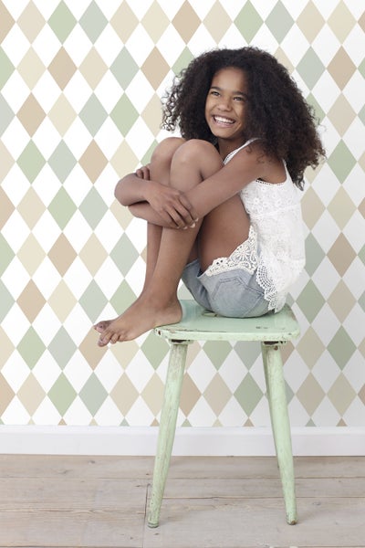 Mädchen sitzt auf Hocker vor Rautenmuster Tapete