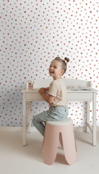 Kind sitzt an einem Schreibtisch vor einer Tapete mit Herzmuster