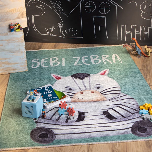 Ein Kinderteppich mit Zebra Motiv und der Aufschrift Sebi Zebra liegt auf einem Boden, umgeben von Spielzeug.