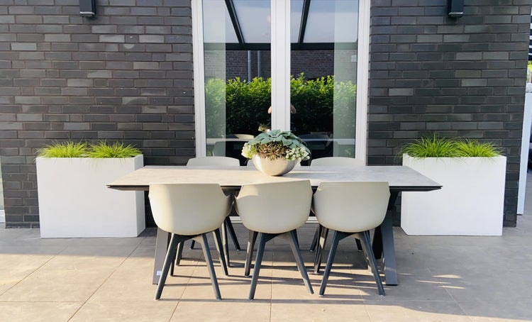 Moderne helle Terrasse mit weißen Pflanzkübeln, grauer Lounge-Garnitur und Holztisch auf Steinboden unter einer weißen Terrassenüberdachung.