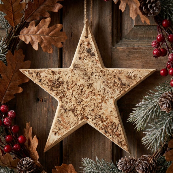Hängender Stern aus Birkenrinde in einem winterlichen Adventskranz aus Eichenblättern, Tannenzapfen und Beeren an einer Holztür