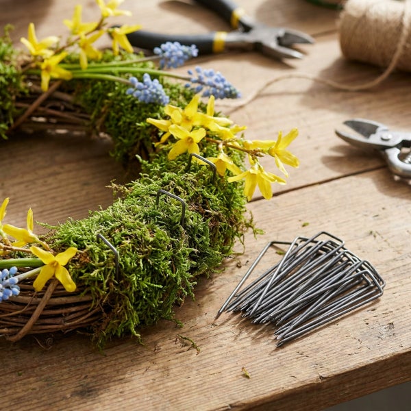 Set aus Drahtklammern fuer Mooskranz auf einem Holztisch mit Bastelwerkzeug und Blumen