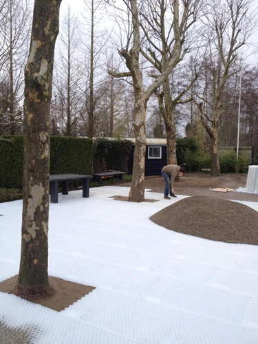 Verlegung von weißen Kiesgittern mit Wabenstruktur auf einer Gartenfläche zur Bodenstabilisierung um Bäume.