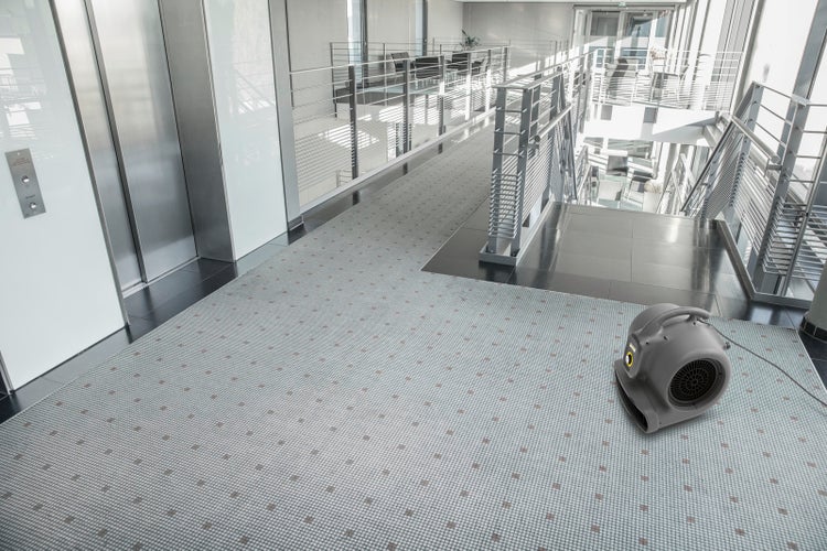 Kärcher Gebläsetrockner in einem modernen, hellen Flur mit Fliesenboden und Metallgeländer neben einem Aufzug.