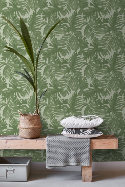 Szene mit grüner Blättertapete, Zimmerpflanze in einem Korb und Kissen auf einer Holzbank.