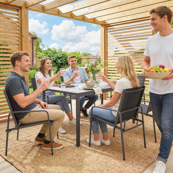 Moderne Garten-Essgruppe mit grauem rechteckigem Tisch und dunklen Stapelsesseln unter einer Pergola aus Holz auf einer hellen Terrasse.