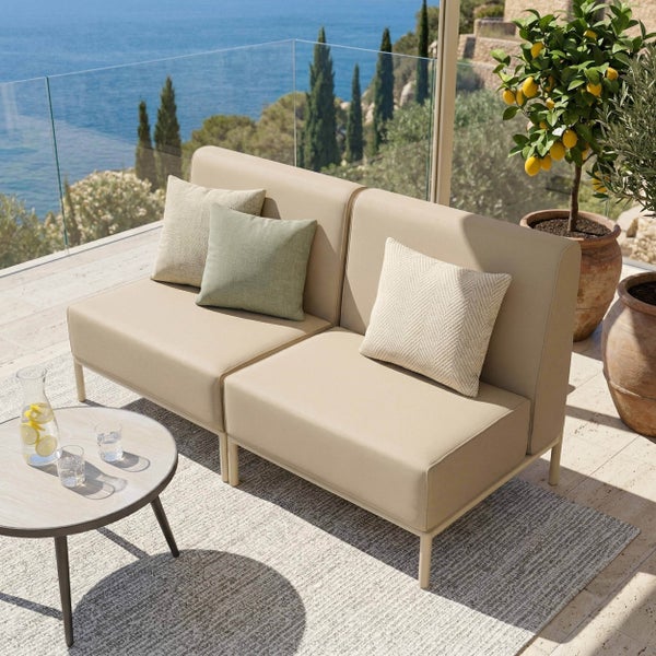 Modernes Lounge-Sofa auf einer hellen Terrasse mit Meerblick, runder Beistelltisch, Teppich und Zitronenbaum im Tontopf.