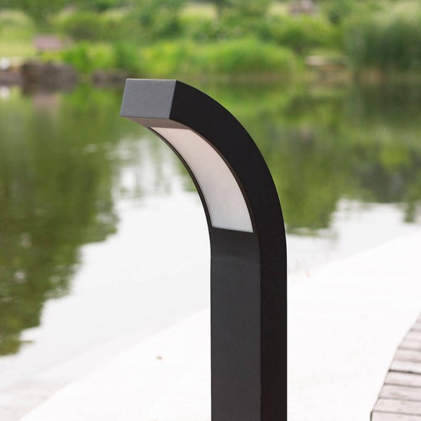 Moderne, schwarze Außenstandleuchte aus Metall mit gebogener Form, platziert an einem Teichufer in einer gepflegten Gartenanlage.