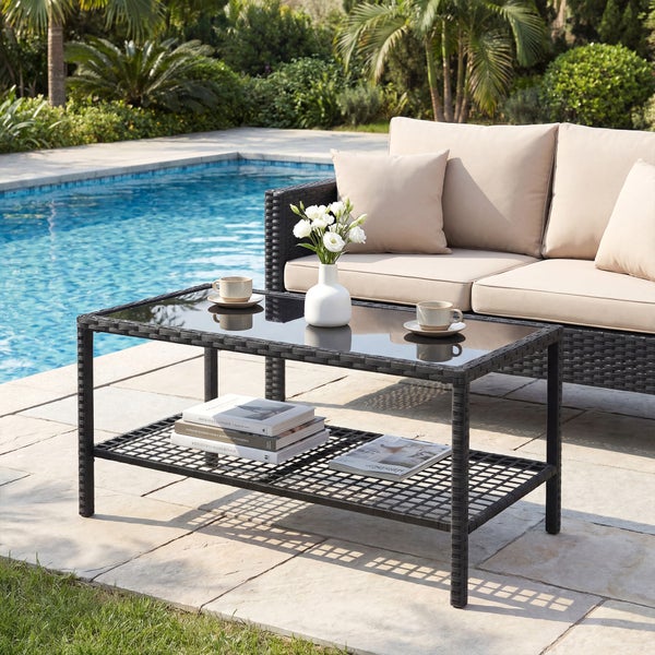 Moderne Gartenlounge mit schwarzem Polyrattan-Couchtisch inklusive Glasplatte und Sofa mit beigen Kissen an einem hellen Poolbereich.
