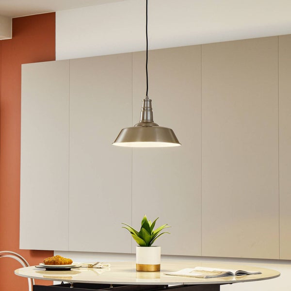 Industrie-Pendelleuchte aus gebürstetem Metall über einem runden Esstisch mit kleiner Pflanze und Buch in hellem Raum.