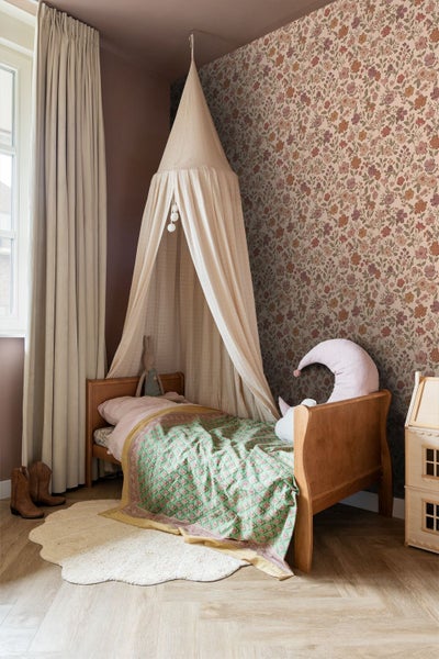 Gemütliches Kinderzimmer mit Holzbett, Baldachin, gemustertem Bettbezug und floraler Tapete an der Wand.