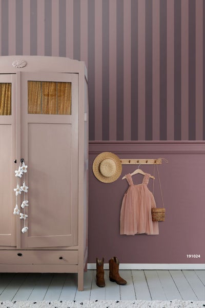 Gestreifte Tapete in Mauve über Wandpaneelen in einem Kinderzimmer mit Kleiderschrank, Garderobenhaken, Strohhut und Kinderkleid.