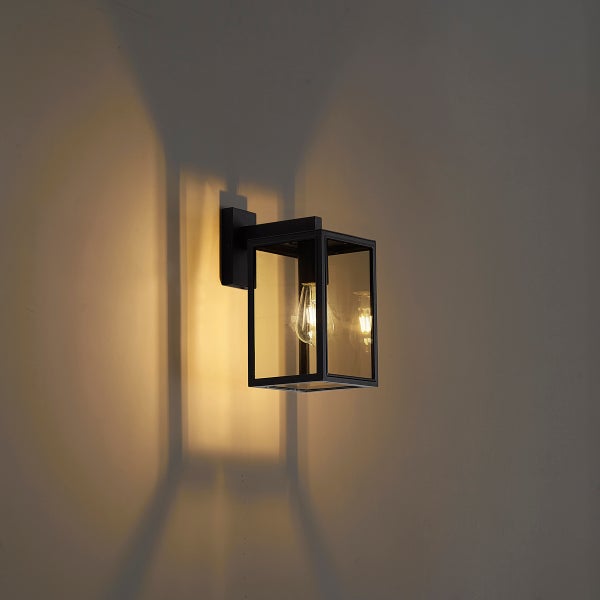 Moderne rechteckige Außenwandleuchte aus schwarzem Metall und Glas mit eingeschaltetem Leuchtmittel an einer Wand.