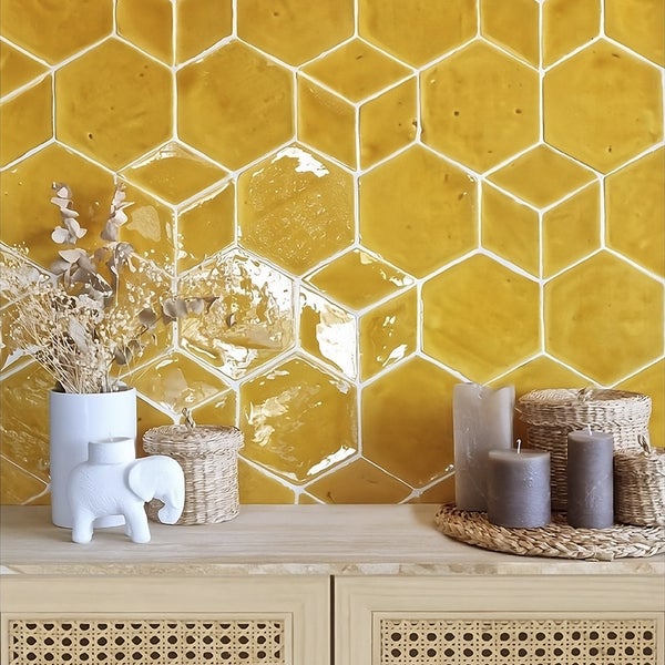Wand mit sechseckigen Fliesen in Honiggelb, davor ein Sideboard mit Kerzen, geflochtenen Körben und einer Vase mit Trockenblumen dekoriert.