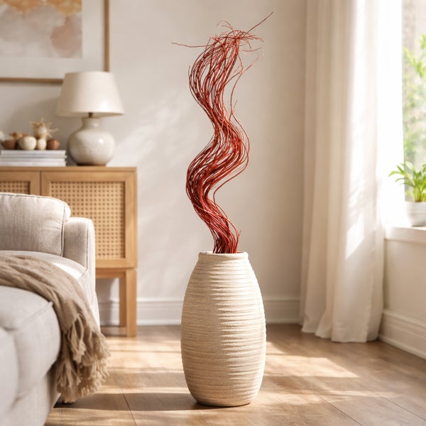 Modernes Wohnzimmer mit strukturierter Bodenvase und hohen, geschwungenen Weidenzweigen. Hell eingerichteter Raum mit Sofa und Holzkommode.
