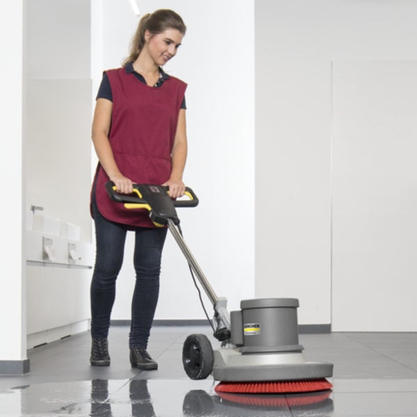Eine Person benutzt eine professionelle Karcher Einscheibenmaschine zur Bodenreinigung in einem gewerblichen Raum.