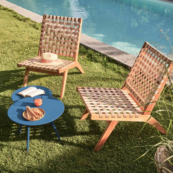Moderne Gartenstühle aus Holz mit Geflecht und ein blauer Beistelltisch auf einer Rasenfläche an einem Pool.