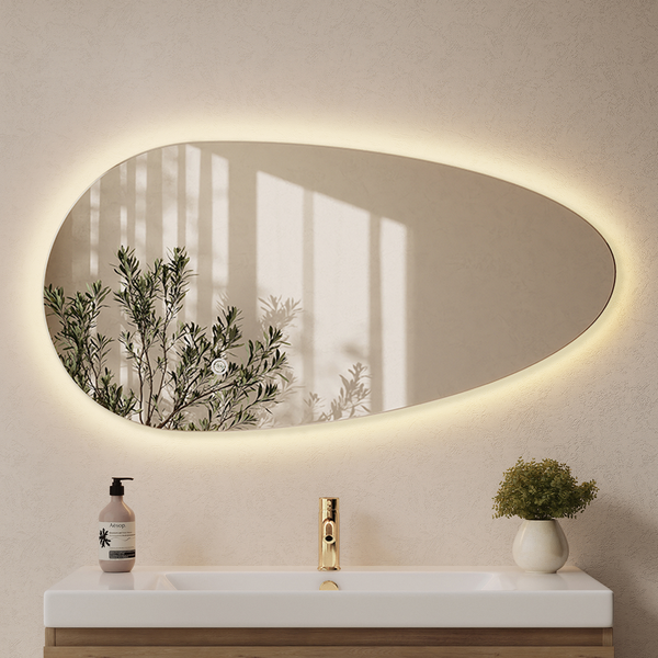 Organisch geformter Wandspiegel mit integrierter LED Beleuchtung über einem Waschbecken mit goldener Armatur in einem modernen Badezimmer.