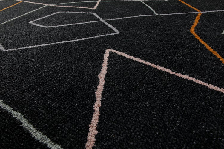Nahaufnahme eines schwarzen kurzflorigen Teppichs mit geometrischem Muster aus weißen, orangefarbenen und rosa Linien.