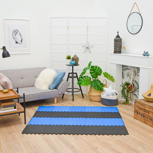 Gestreifte Puzzlematte aus Schaumstoff in Blau und Schwarz, ausgelegt in einem hell eingerichteten Wohnzimmer mit Sofa und Pflanzen.