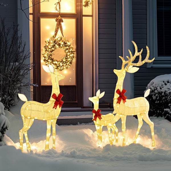 Drei beleuchtete LED-Rentierfiguren mit roten Schleifen stehen im Schnee vor einem Hauseingang mit einem leuchtenden Weihnachtskranz.