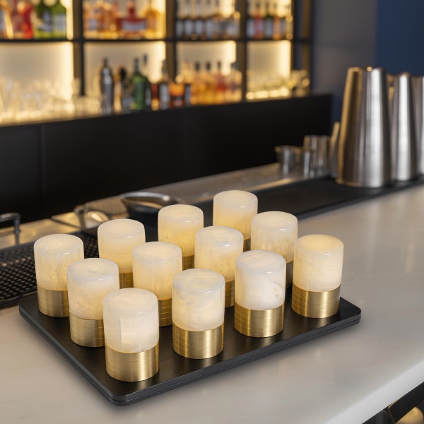 Mehrere kabellose LED-Tischleuchten mit Marmorschirm und goldfarbenem Sockel auf einem Tablett in einer Bar mit warmer Beleuchtung.