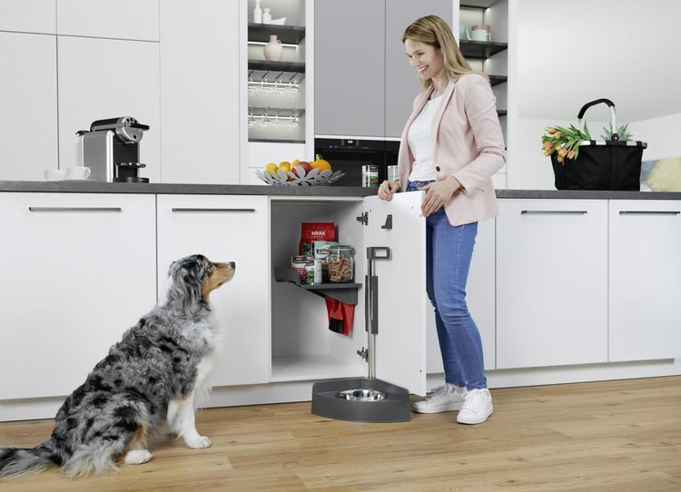Moderne helle Küche mit einem Unterschrank-Auszug für Tiernahrung und integriertem Futternapf sowie einer Frau und einem Hund.